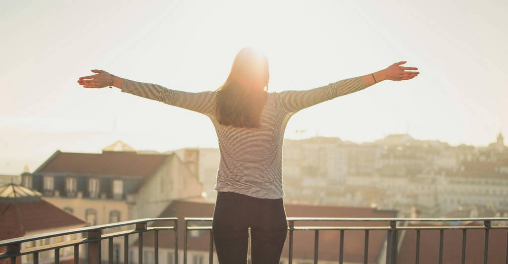 A woman stands on a balcony with arms wide open in the morning light, capturing the essence of self care and reclaiming mental health through intentional living.