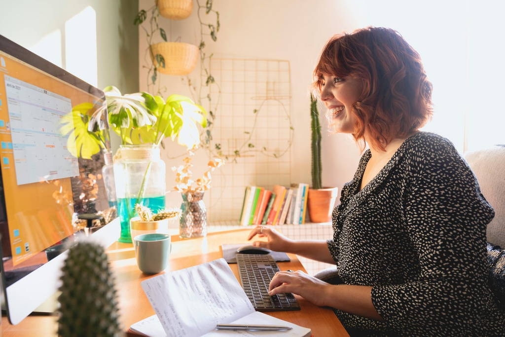 Smiling professional working in a bright, plant-filled home office, representing mental clarity and work-life balance.