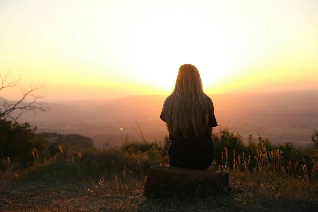 A person watches the sunrise from a quiet mountaintop, symbolizing a journey toward life satisfaction and the freedom to break free from societal pressures.