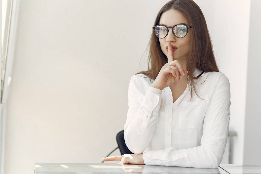 A woman in glasses placing her finger on her lips, symbolizing the power of silence and self-reflection.