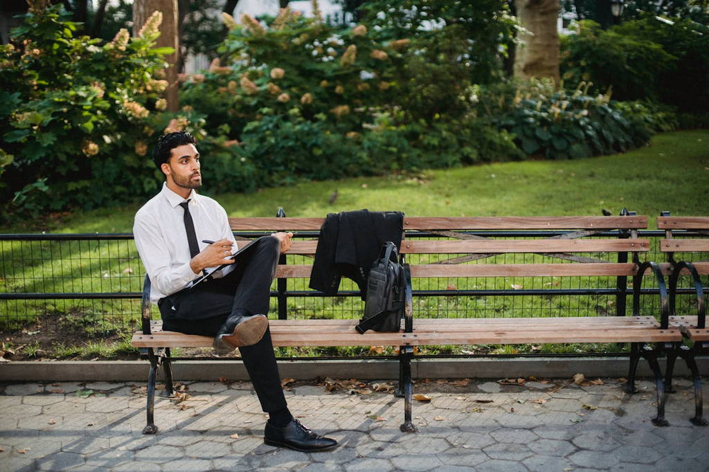 A professional man sitting on a park bench, engaged in silent contemplation and deep thinking.