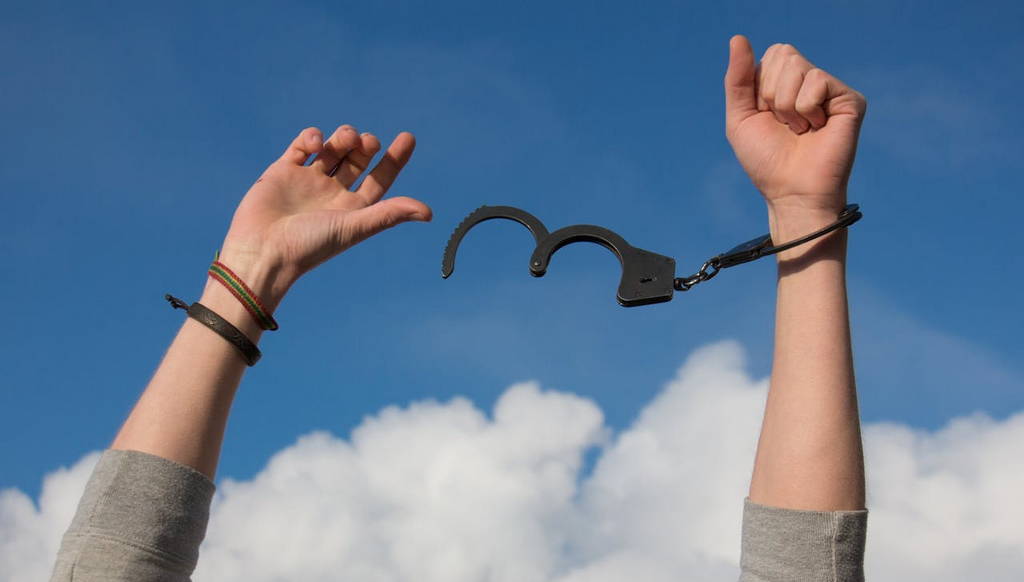 A person breaking free from handcuffs against a blue sky, symbolizing career freedom and overcoming obstacles.