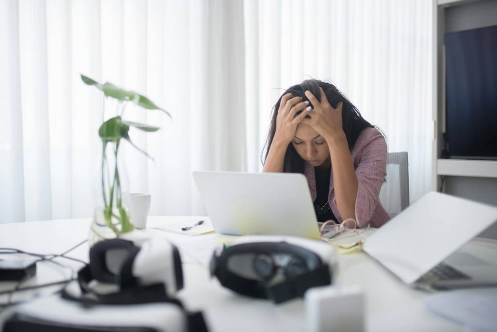 A woman sits at a desk with her head in her hands, overwhelmed by negative thoughts and work-related stress, highlighting the urgent need to prevent burnout and prioritize mental health.