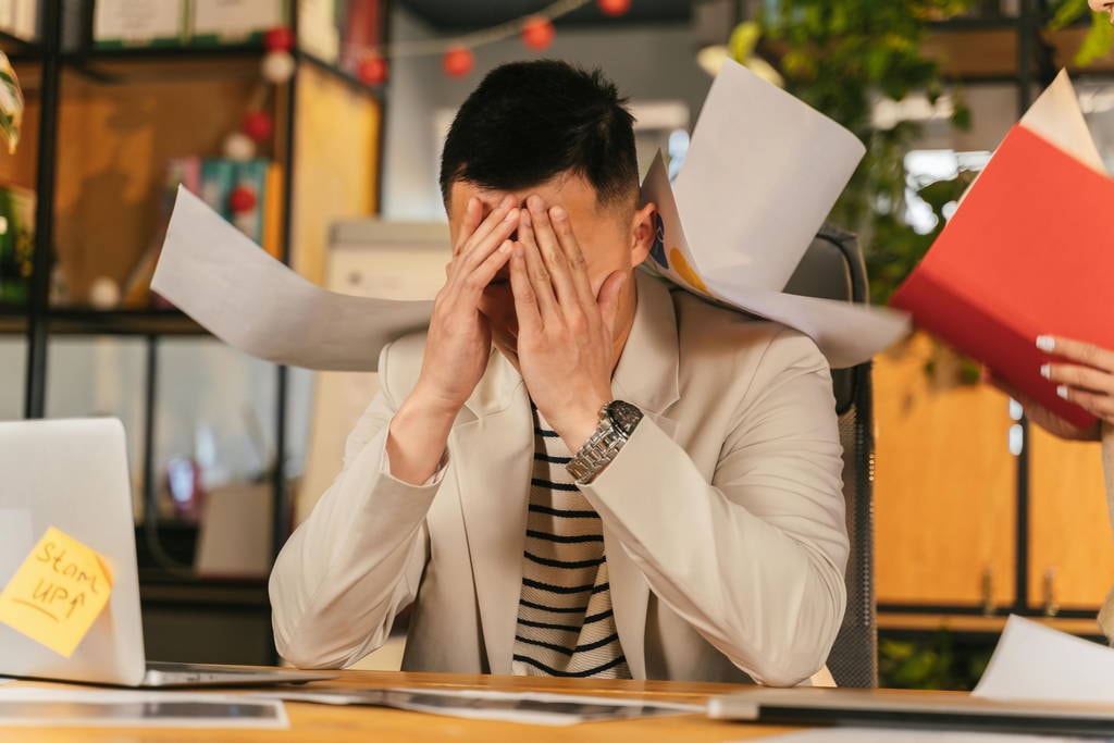Stressed executive covering his face amid a flurry of documents, illustrating cognitive overload at work.
