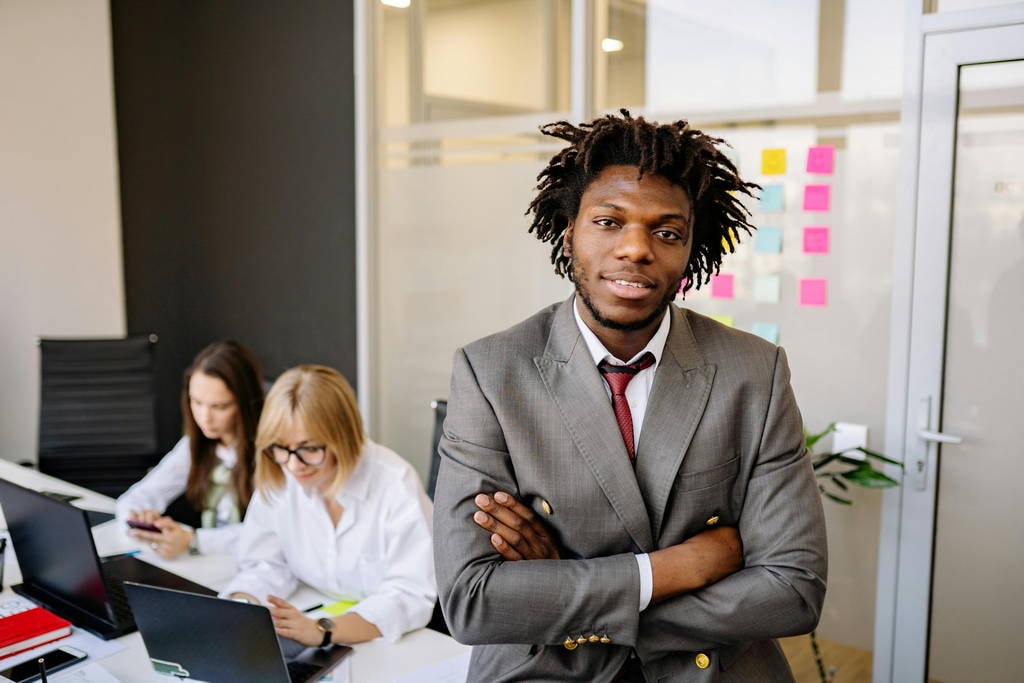 Confident young business leader standing in front of diverse team, embodying traits of a great leader through reflective leadership.