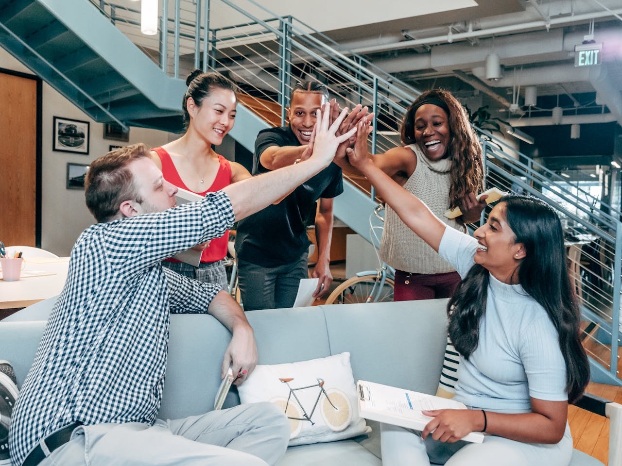 Diverse team high-fiving in an office, celebrating collaboration and inclusion in a psychologically safe workplace.