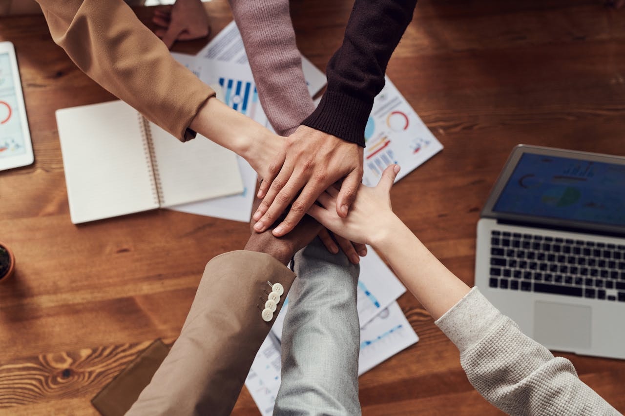 Hands of a diverse team stacked together over business documents, symbolizing trust and teamwork in a high-performing team.