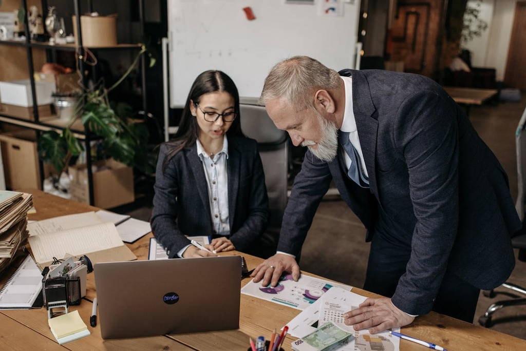 A senior executive assertively guiding a young professional through strategic decisions, demonstrating leadership dynamics and workplace influence.
